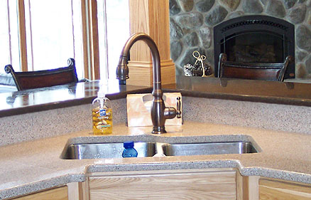 An undermount double bowl stainless steel corner kitchen sink in combination with quartz counters, bronze faucet and wood cabinets