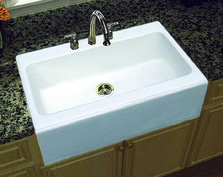 An apron front single bowl white cast iron kitchen sink in combination with granite counters and wood cabinets