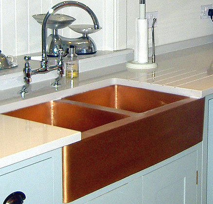 An apron front double bowl copper kitchen sink in combination with white backsplashes, countertops and cabinets