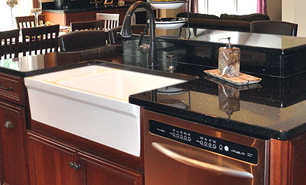 White porcelain kitchen farmhouse sink in combination with black granite countertops and cherry cabinets