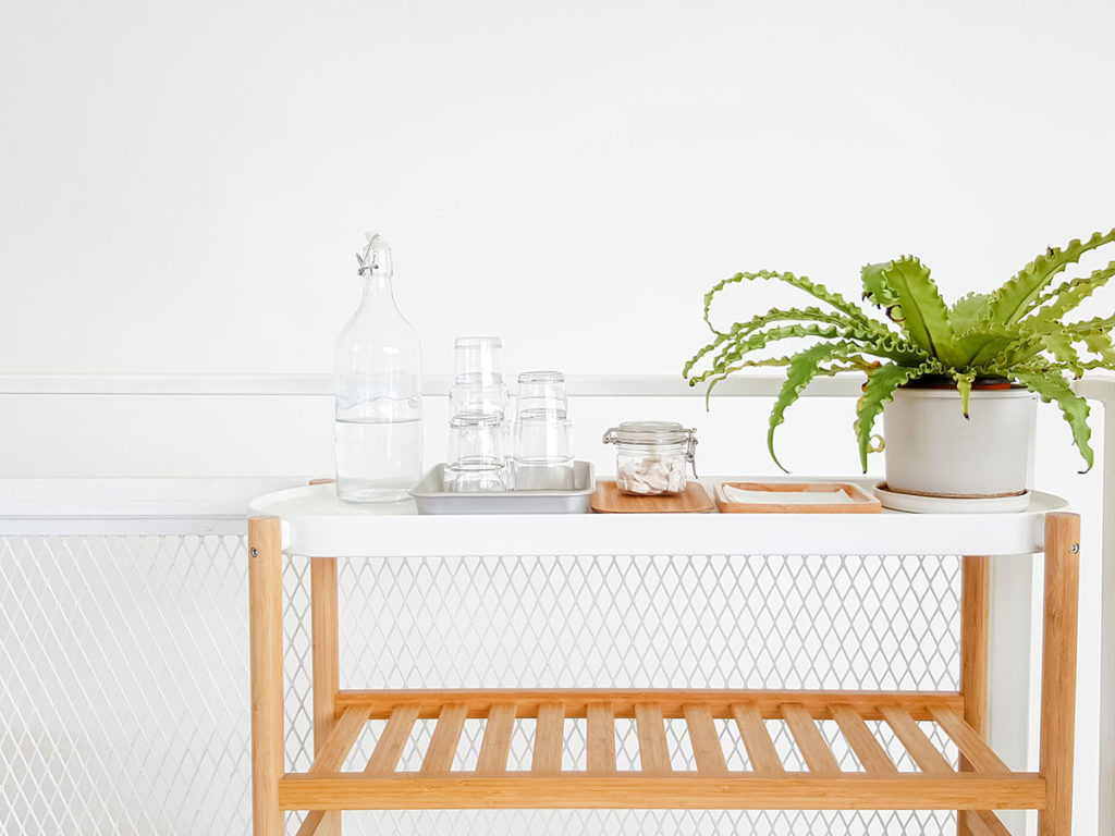 A bottle of water and a green flower on a wooden table in a hotel white room.